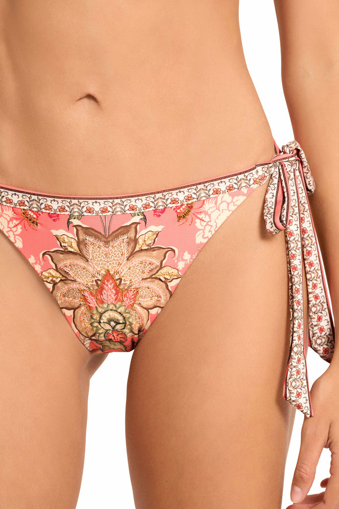 A close up look of a model wearing the Spirit Tie Side Bikini Bottom, with adjustable tie side and cheeky bottom coverage, adorned with pink floral print.